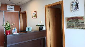 Un área de recepción con un mostrador de madera, una planta en maceta, un cuadro enmarcado y un letrero en la pared.