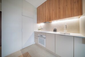 A modern kitchen with white cabinetry, a wooden upper section, a built-in oven, and a stainless steel sink. - Kierbedzia Apart (Warszawa)