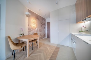 A modern kitchen with a herringbone floor pattern, wooden cabinets, and a dining area with a round table and chairs. - Kierbedzia Apart (Warszawa)