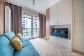 A modern living room with a sofa, a flat-screen TV, and large windows. - Kierbedzia Apart (Warszawa)