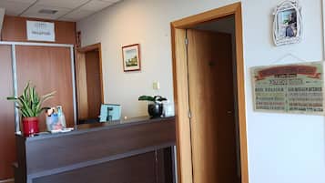 Un área de recepción con un mostrador de madera, una planta en maceta, un cuadro enmarcado y un letrero en la pared.
