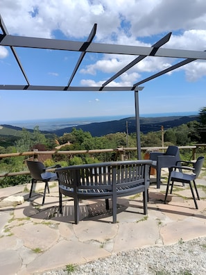 A bench and chairs under a pergola with a view of a landscape.