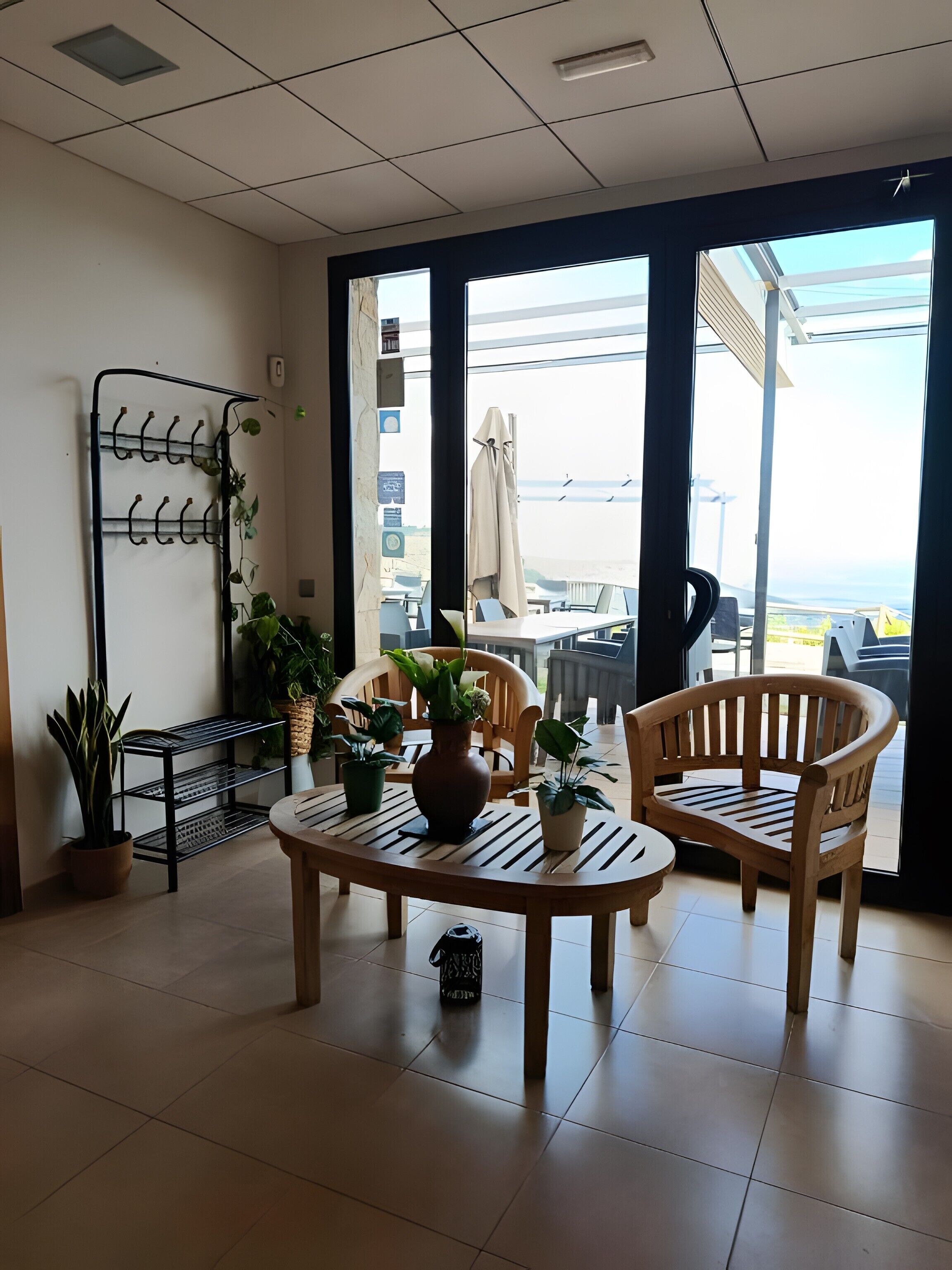 Une pièce avec une table et deux chaises, une étagère pour les plantes et une vue sur l’extérieur.