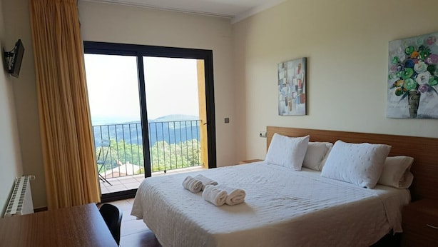 A hotel room with a large bed, a view of the outdoors, a painting on the wall, and a window with curtains. - Room 'Habitació Alzina' with Sea View, Balcony and Wi-Fi (Mont-ral)
