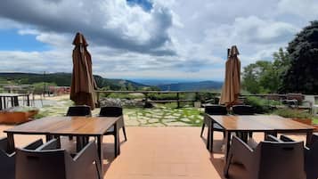 An outdoor terrace with tables and chairs, a view of the landscape, and a cloudy sky.