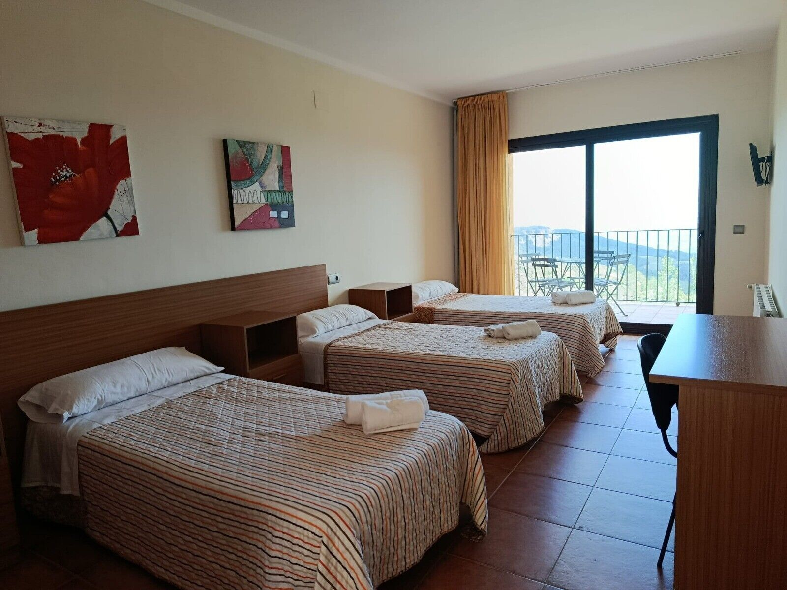 A hotel room with three beds, a dining table, and a balcony with a view.