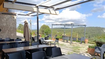 An outdoor patio with tables and chairs, a stone wall, and a view of the landscape.