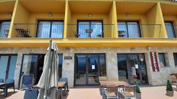 Un bâtiment jaune avec une enseigne indiquant la présence d’un restaurant, des tables à l’extérieur et un espace d’accueil.