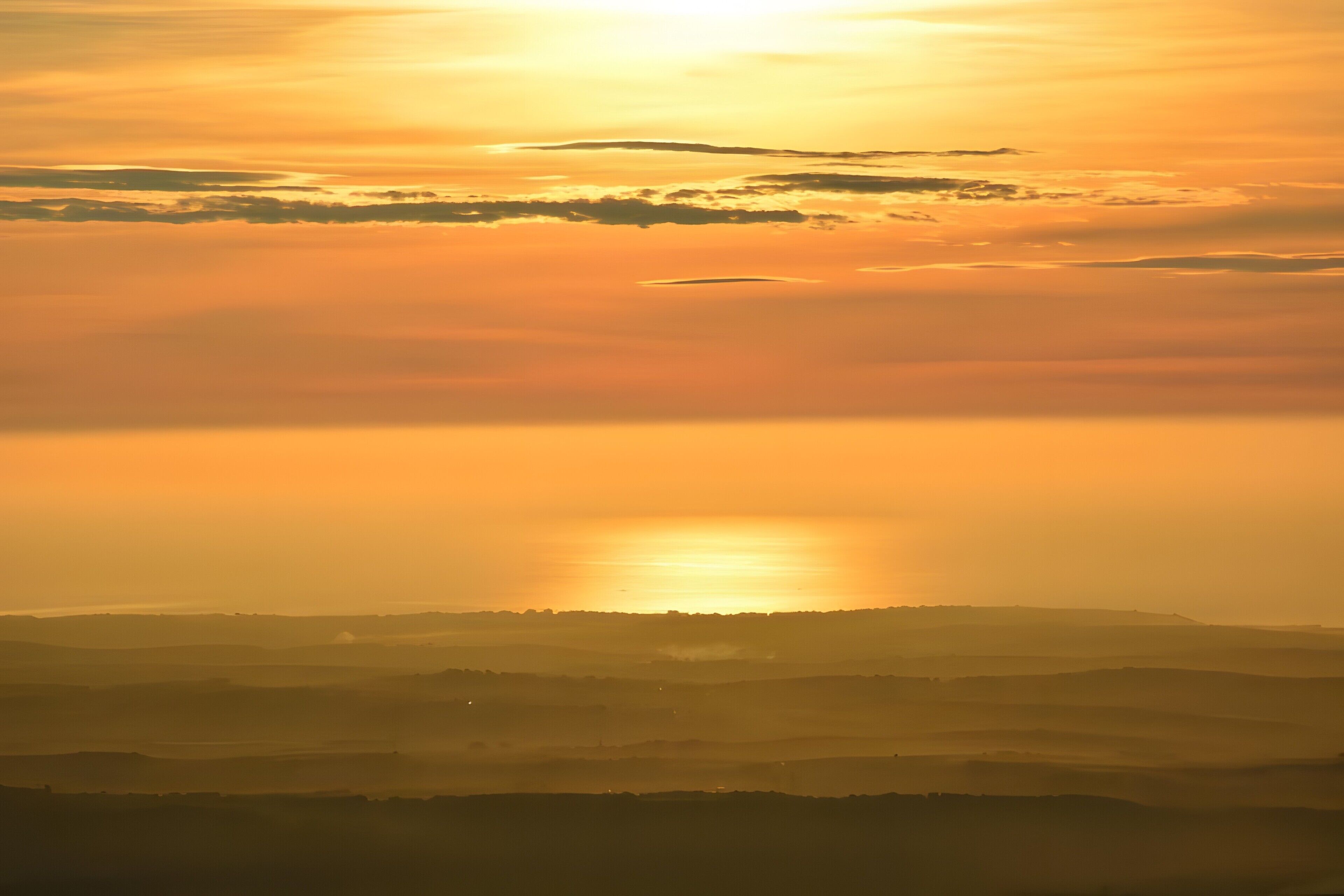Un paisaje con el sol poniéndose o saliendo sobre una serie de colinas.