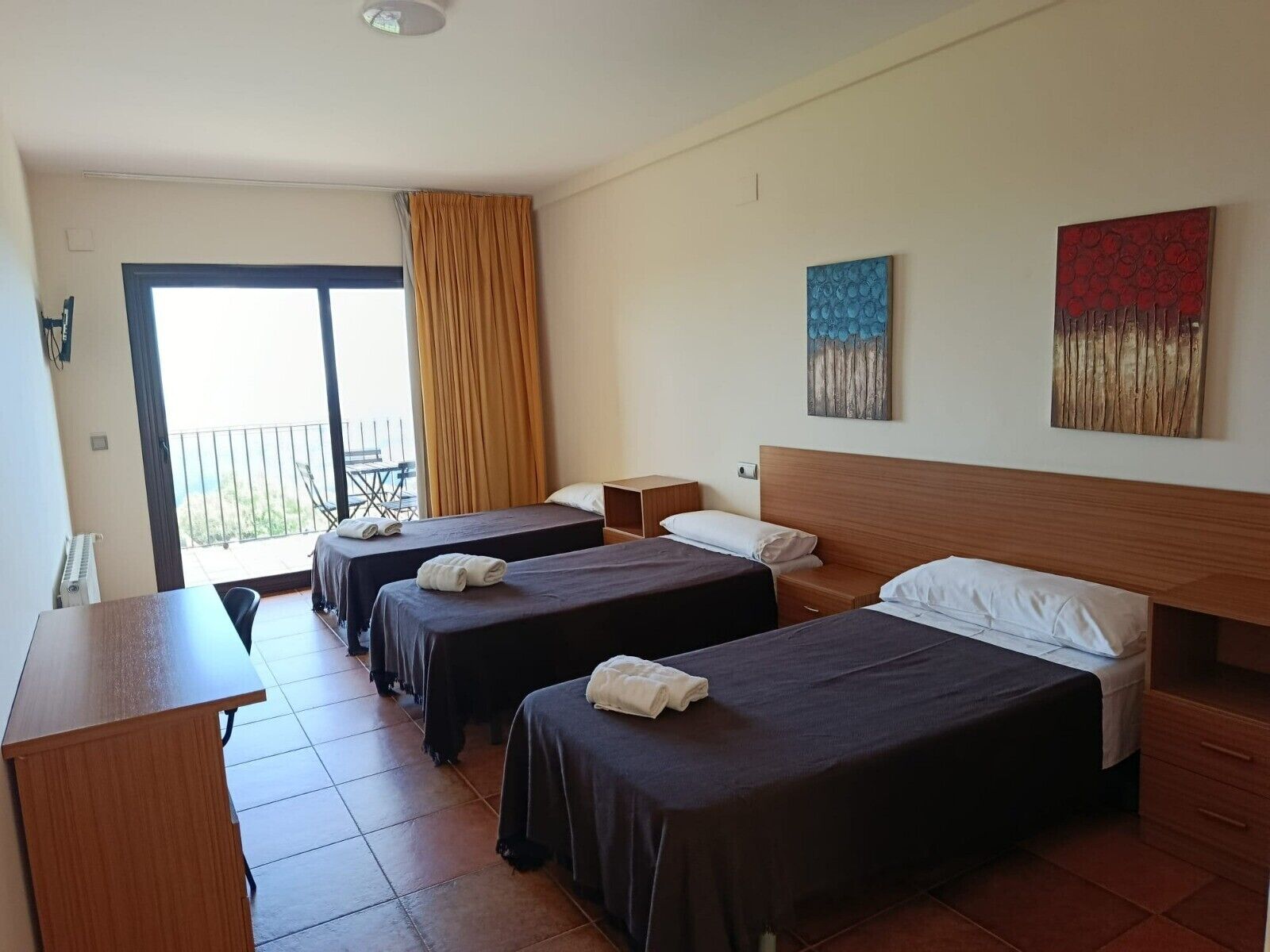 A hotel room with two beds, a desk, and a balcony with a view.