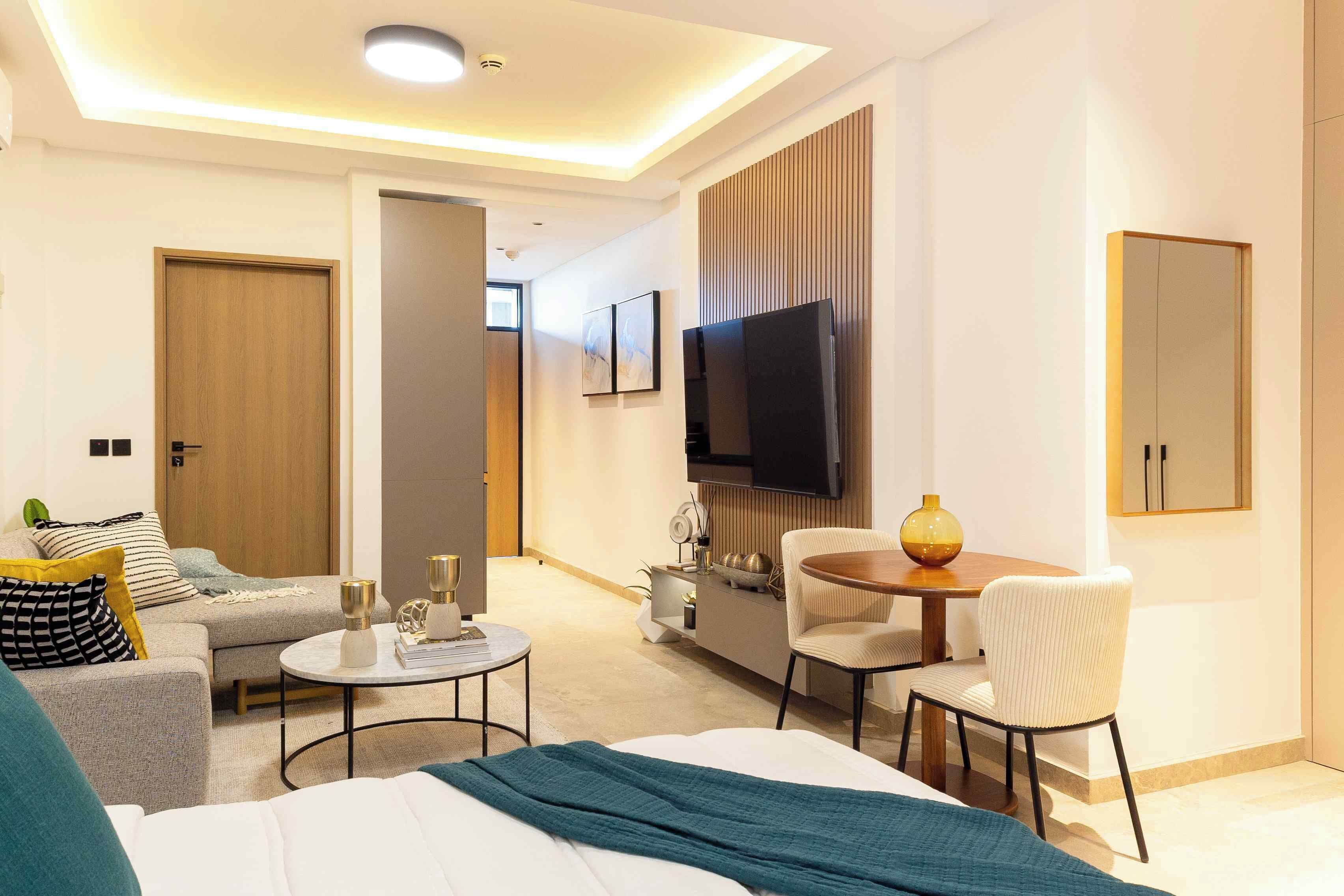A hotel room with a bed, a sofa, a dining table, and a TV.