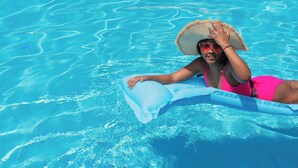 A person in a swimming pool with clear blue water, wearing a pink swimsuit and a straw hat. - KORE -The Milton (Accra)