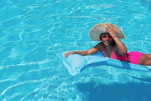 A person in a swimming pool with clear blue water, wearing a pink swimsuit and a straw hat. - KORE -The Milton (Accra)