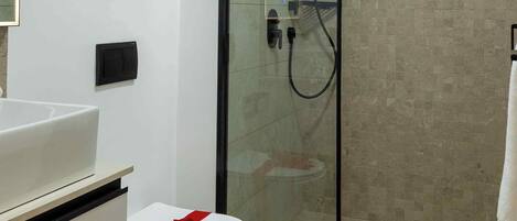 A modern bathroom with a glass-enclosed shower, a white toilet with a red ribbon, and a framed abstract painting on the wall.