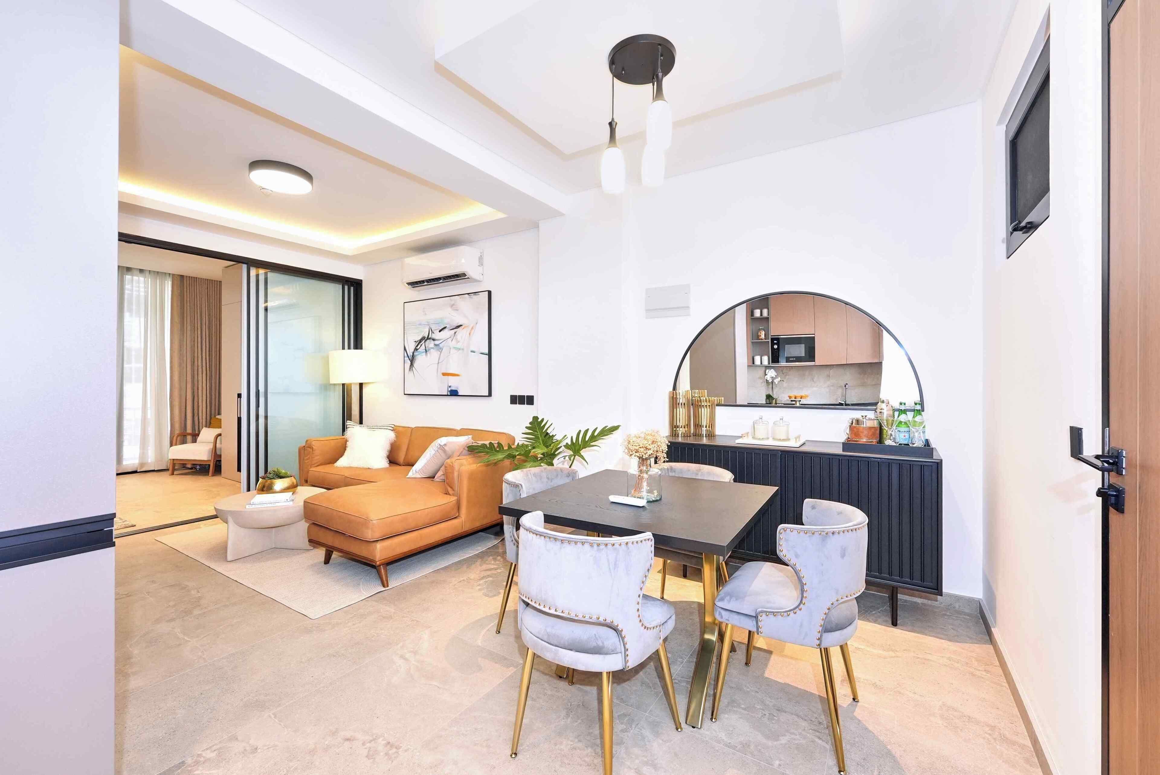 Un salon moderne comprenant un canapé, une table basse et des fauteuils, un coin repas avec une table et des chaises, et une cuisine équipée d’un four à micro-ondes et de placards.