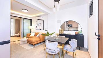 Un salon moderne comprenant un canapé, une table basse et des fauteuils, un coin repas avec une table et des chaises, et une cuisine équipée d’un four à micro-ondes et de placards.