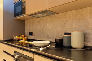 A modern kitchen with a Bosch microwave, a wooden fruit basket, a white frying pan, and a set of black and white containers. - KORE -The Milton (Accra)