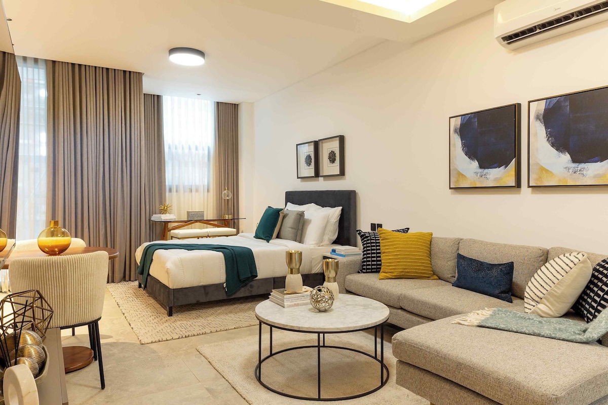 A modern hotel room with a bed, a sofa, a round coffee table, and artwork on the walls.