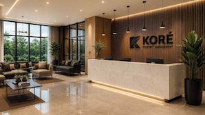 A modern reception area with a marble counter, wooden paneling, and a large window offering a view of greenery. - Bravia Residency - Spring Properties (Accra)