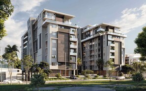 Een modern appartementencomplex met meerdere verdiepingen, balkons, een aangelegde tuin en een heldere lucht.