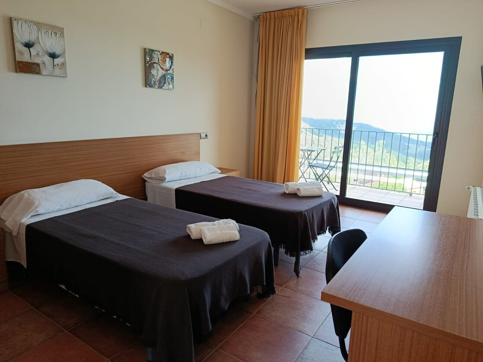 A hotel room with two beds, a wooden desk, and a balcony with a view.