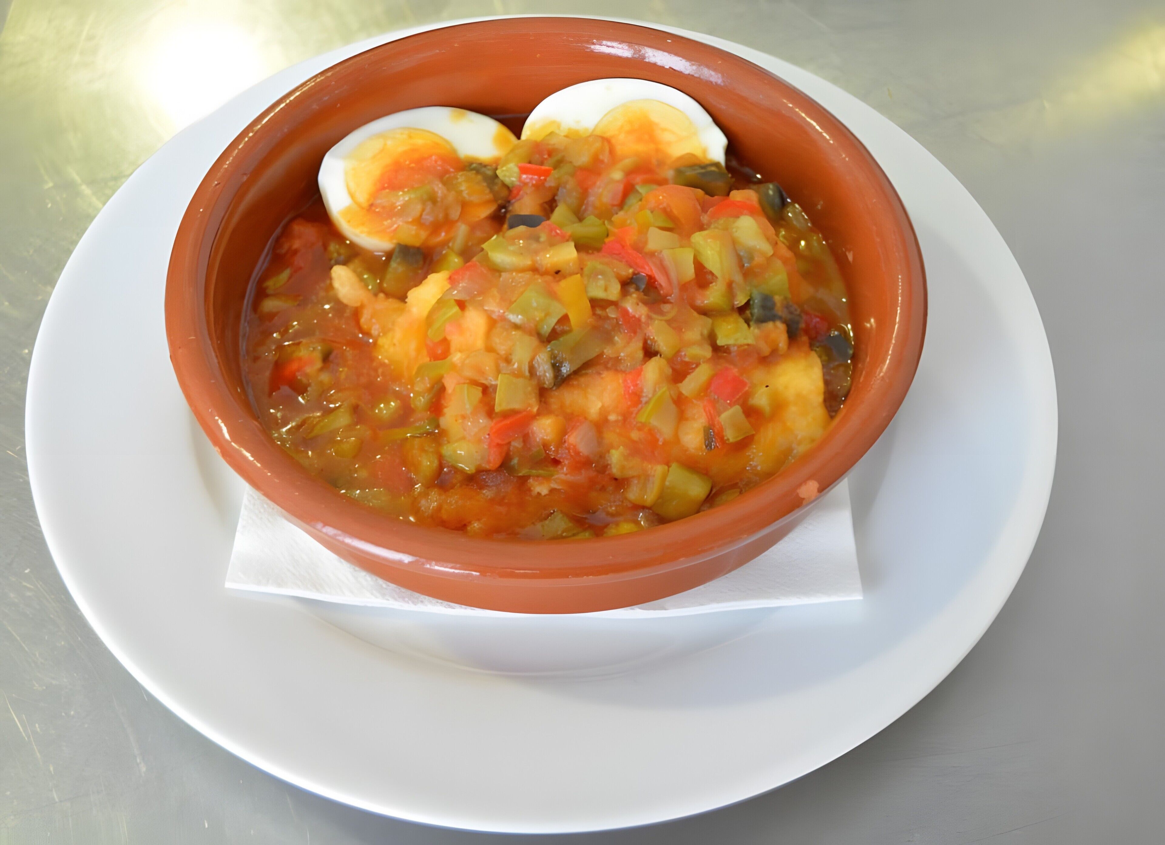 Un plato blanco con sopa, verduras y un huevo duro.
