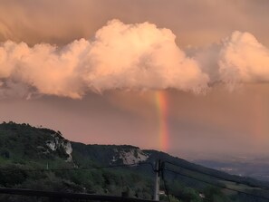 A landscape with a mountain range, a rainbow, and a cloudy sky.