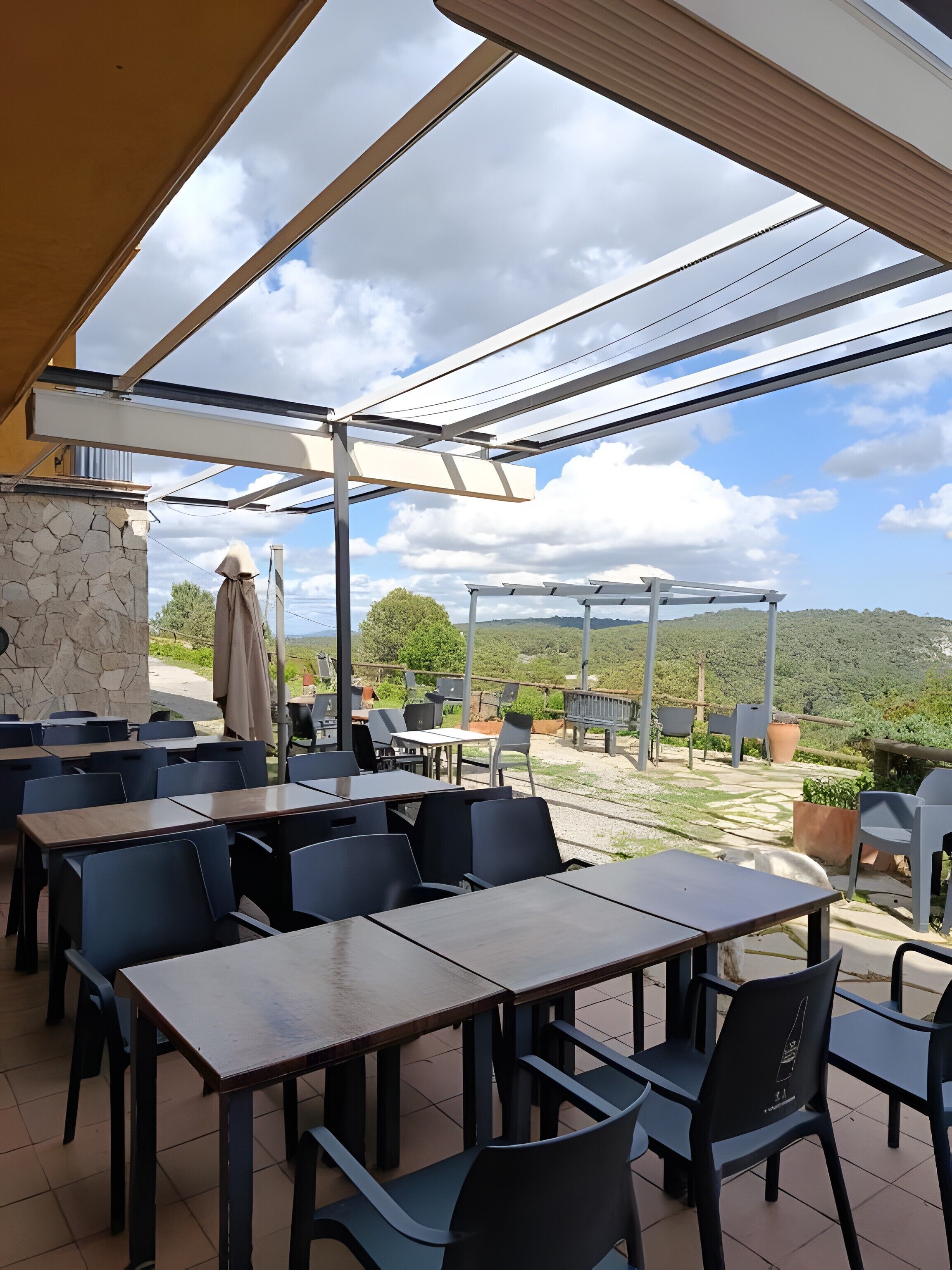 An outdoor patio with tables and chairs, a stone wall, and a view of the landscape.