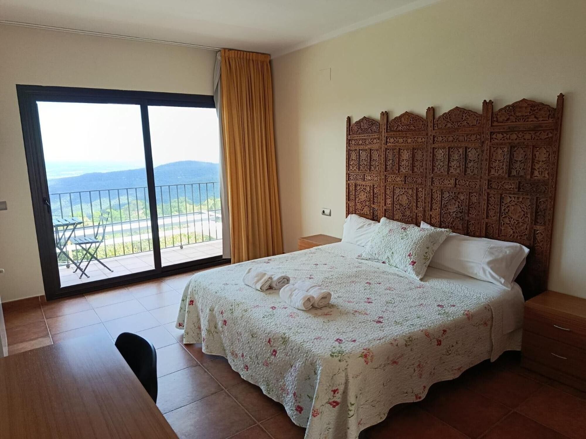 A bedroom with a bed, a nightstand, a wooden headboard, a balcony with a view, and a sliding glass door.