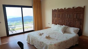 A bedroom with a bed, a nightstand, a wooden headboard, a balcony with a view, and a sliding glass door.