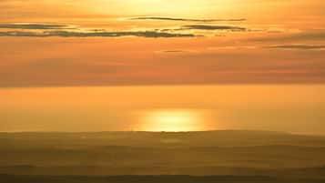 A landscape with a sun setting or rising over a series of hills.