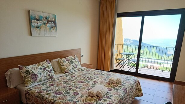A hotel room with a bed, a painting, a balcony with a view, and a chair. - Room 'Habitació Noguer' with Sea View, Balcony and Wi-Fi (Mont-ral)