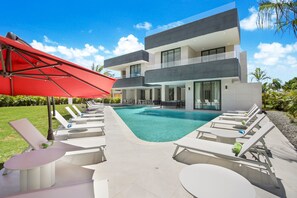 Un bâtiment moderne à deux étages, doté d’une piscine, de chaises longues et d’un parasol rouge.