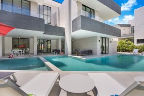 A modern residential building with a swimming pool, outdoor seating, and a clear sky. - Brand New Villa Las Palmas in Cap Cana With Chef Pool Jacuzzi 2 Golf Carts (Punta Cana)
