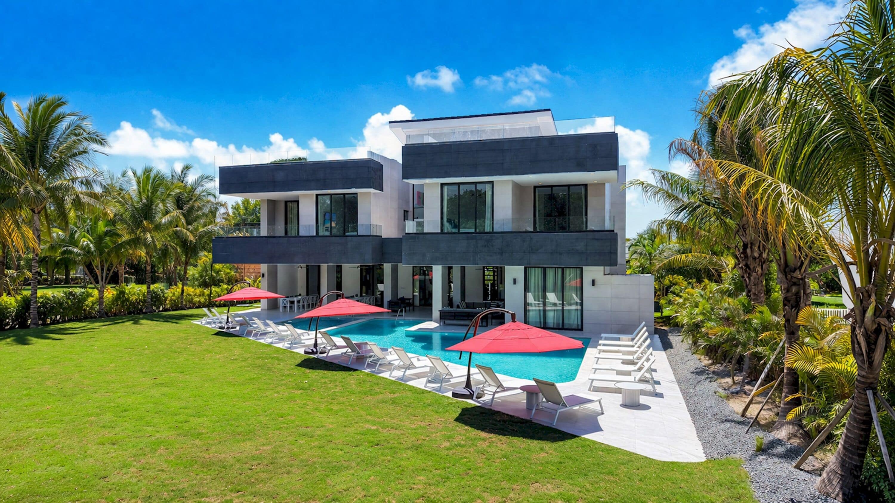 Une maison moderne à deux étages, dotée d’une piscine, entourée de palmiers et d’une pelouse bien entretenue.