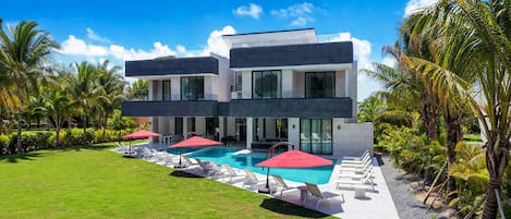 Een modern herenhuis met zwembad, omringd door palmbomen en een verzorgd gazon.