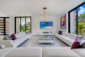 Un salon moderne avec des canapés blancs, une table basse en verre et une grande fenêtre donnant sur un paysage verdoyant.