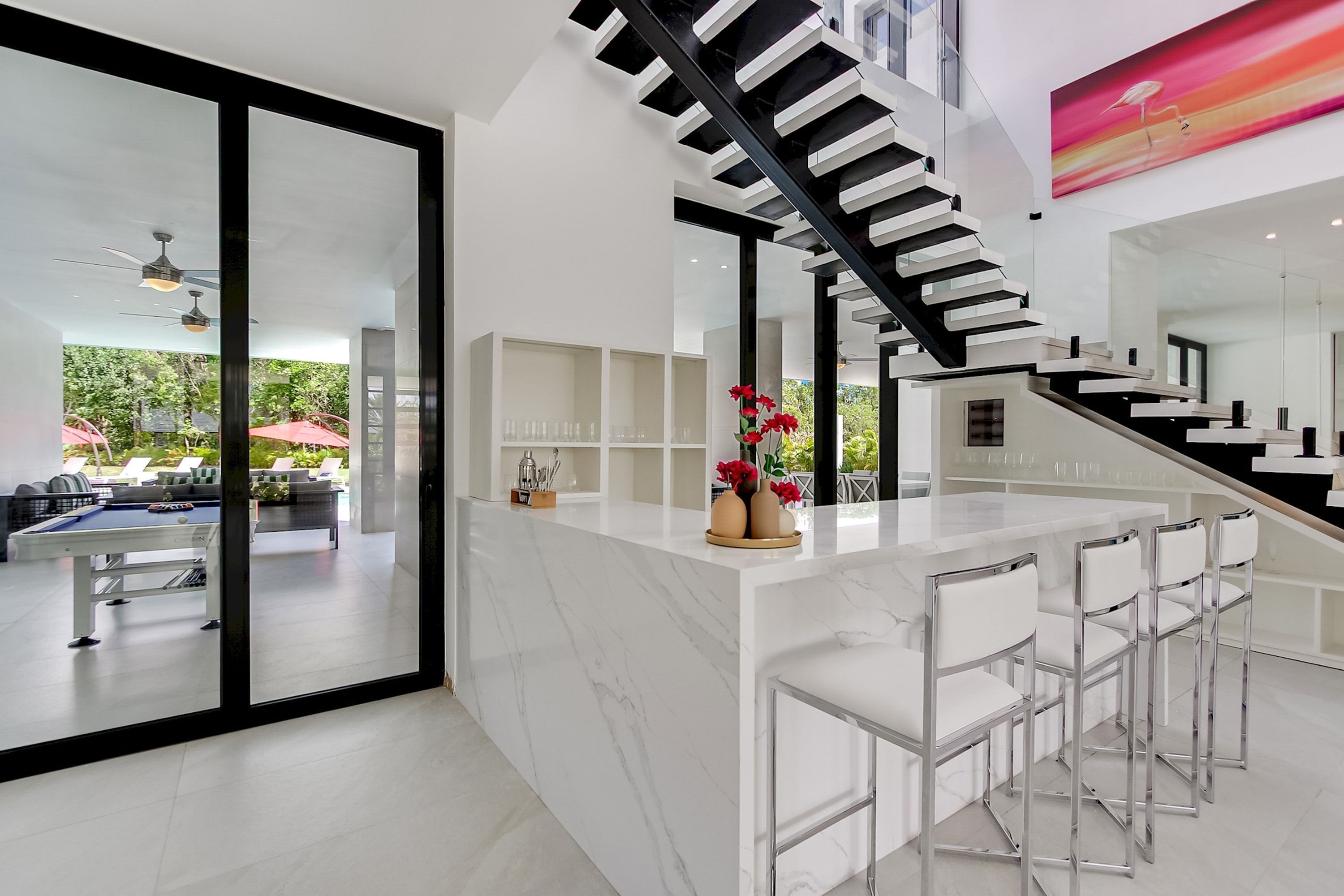 A modern kitchen with a marble countertop, a black staircase, and a dining area with white chairs.