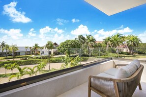 Un balcon avec un fauteuil en osier et une vue sur un quartier résidentiel, avec des maisons et des palmiers.