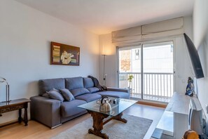 A living room with a sofa, a glass coffee table, a painting on the wall, and a TV on the wall. - Wake up to a view of the Sagrada Familia (Barcelona)