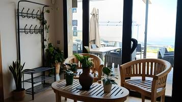 Una habitación con una mesa, dos sillas, una estantería con plantas y vistas al exterior.