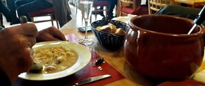 Una mesa de comedor con un plato de sopa, un vaso de agua, una cesta de pan y una taza de cerámica grande.