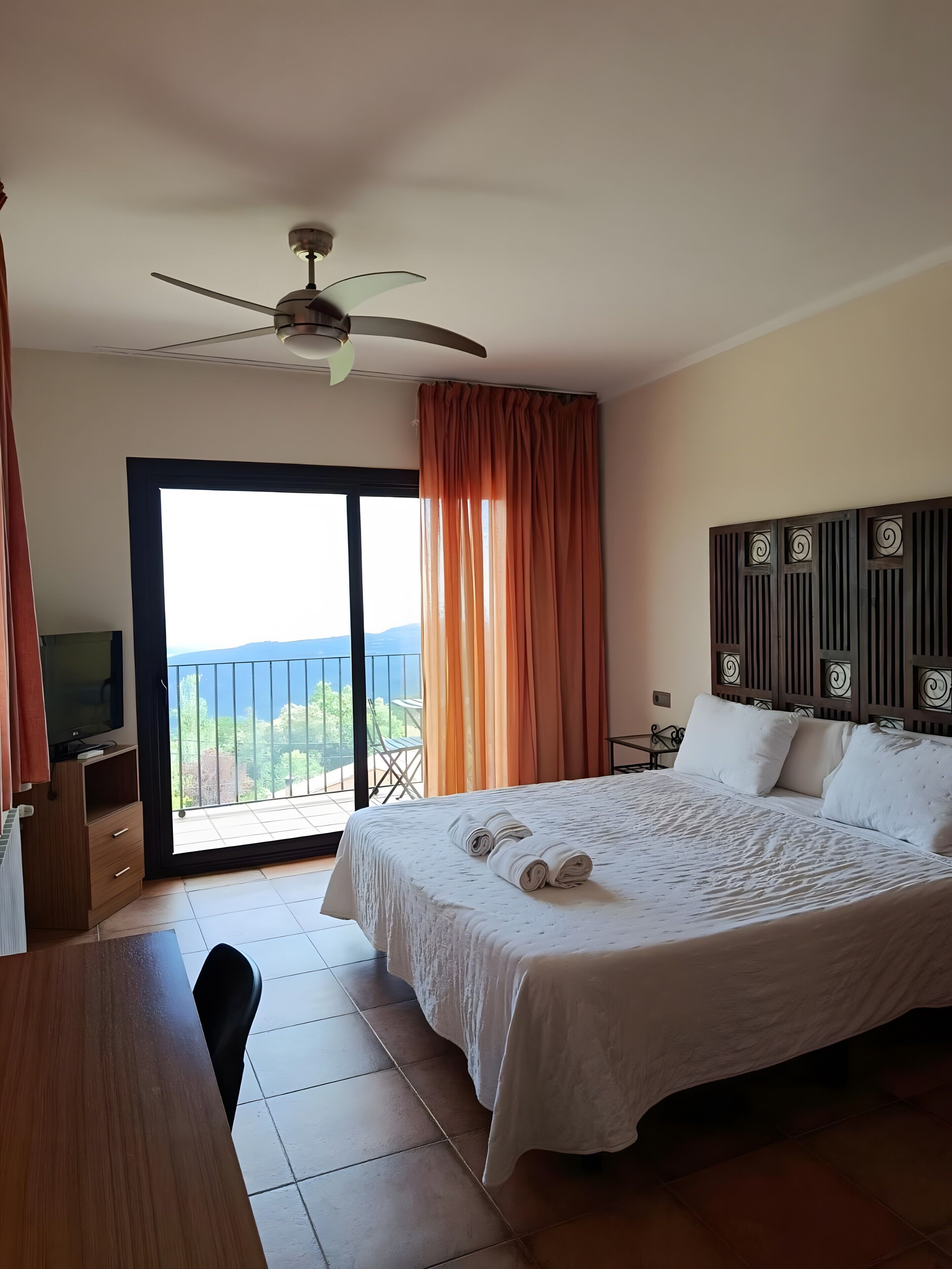 A hotel room with a bed, a television, a desk, and a balcony with a view.