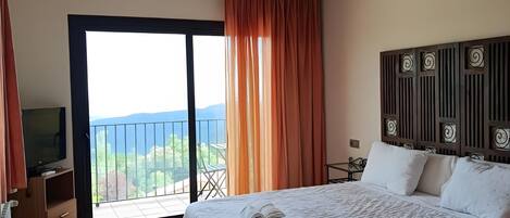 A hotel room with a bed, a television, a desk, and a balcony with a view.