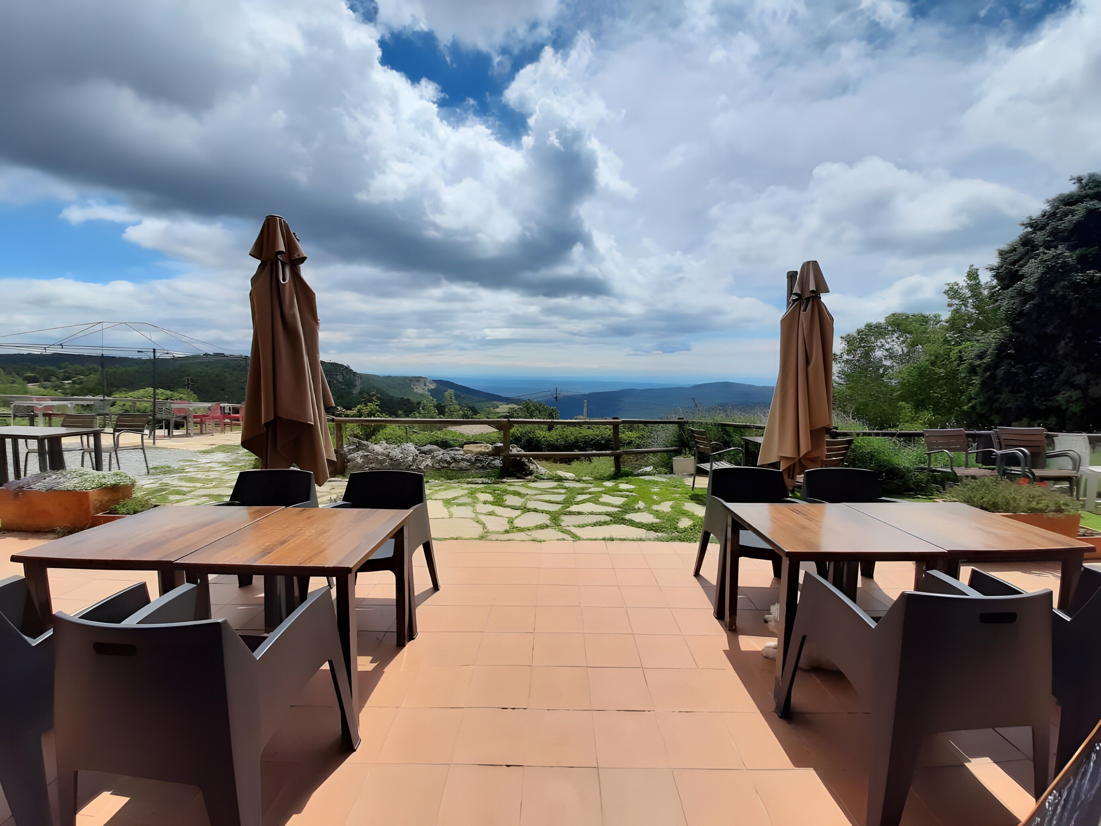 An outdoor terrace with tables and chairs, a view of the landscape, and a cloudy sky.