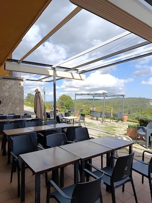 An outdoor patio with tables and chairs, a stone wall, and a view of the landscape. - Room 'Habitació Pi' with Sea View, Balcony and Wi-Fi (Mont-ral)