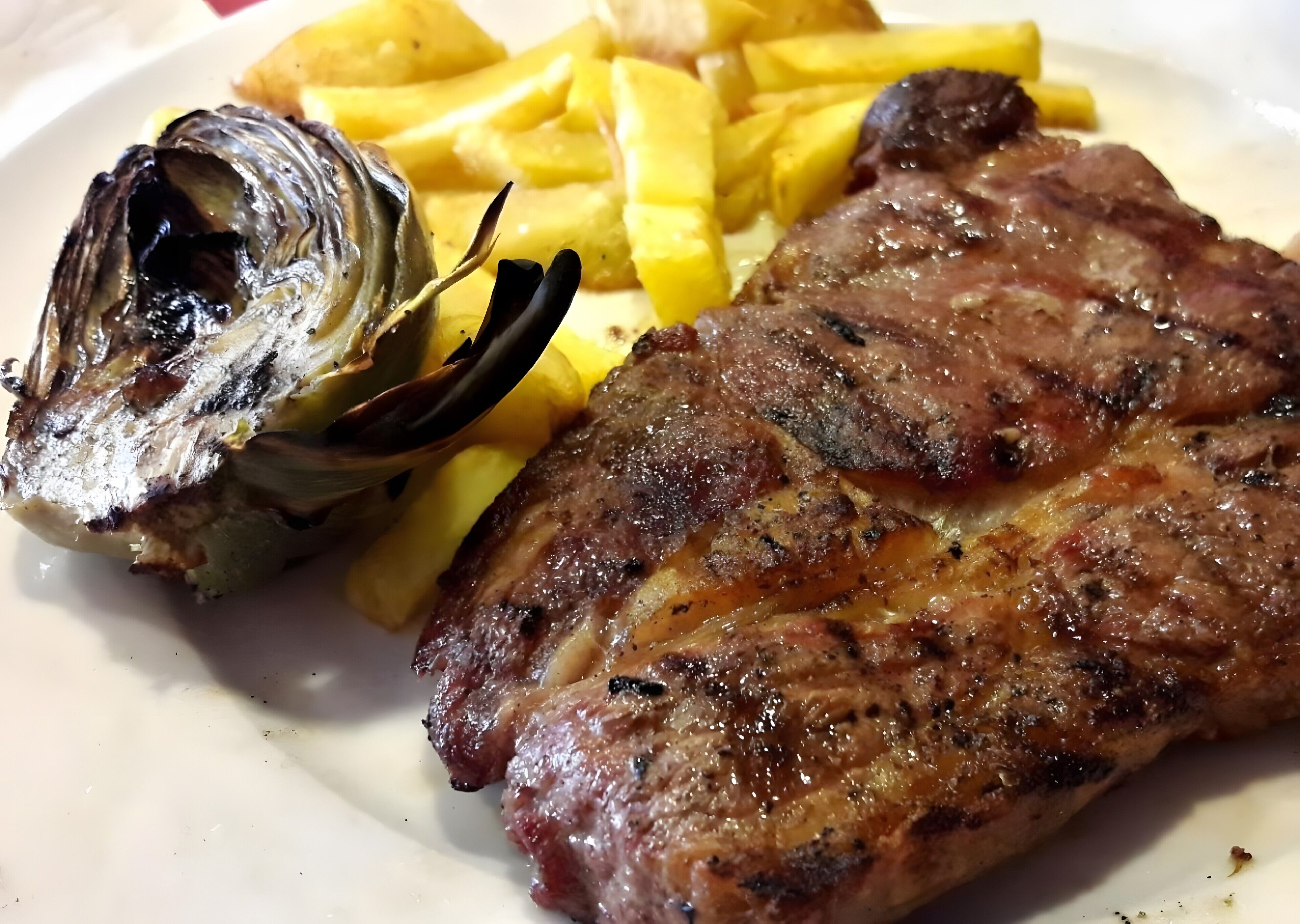 Un plato con bistec a la parrilla, papas fritas y alcachofa asada.