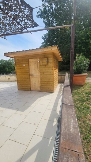 A wooden structure with a door and windows, situated on a tiled patio with a grassy area and a potted plant nearby. - Vrbo Property (Agonac)