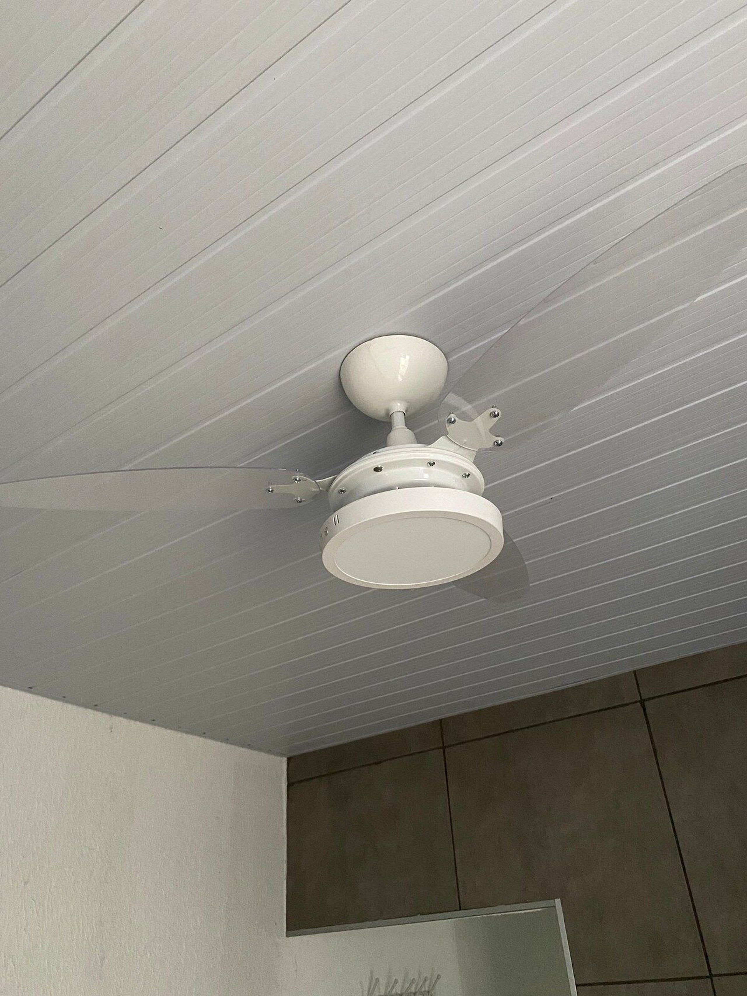 Un ventilador de techo en una habitación con piso de baldosas y un espejo colgado en la pared.