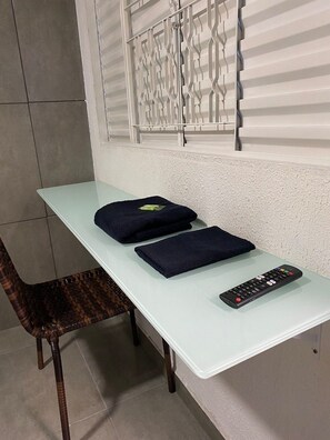 A room with a light-colored table, two dark cushions, a remote control, and a wicker chair.
